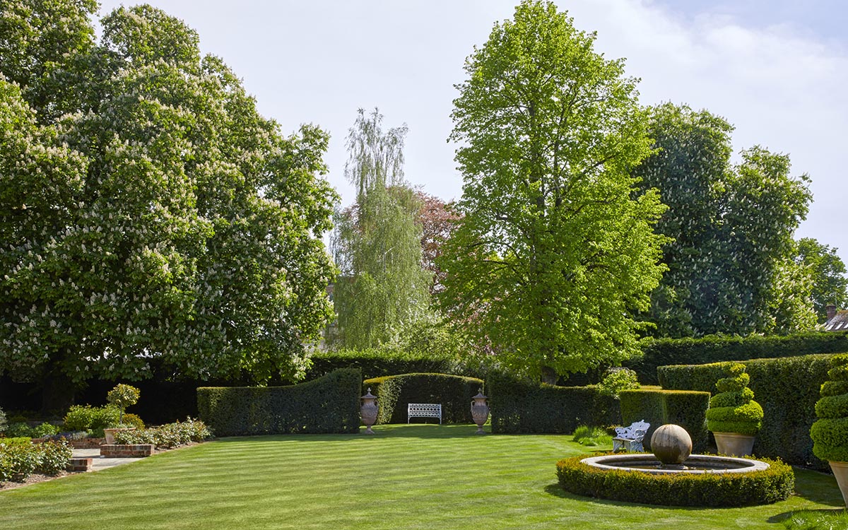 Expansive striped lawn framed by large trees and yew hedging with a formal pond in memory of Mary's friend Penny. 