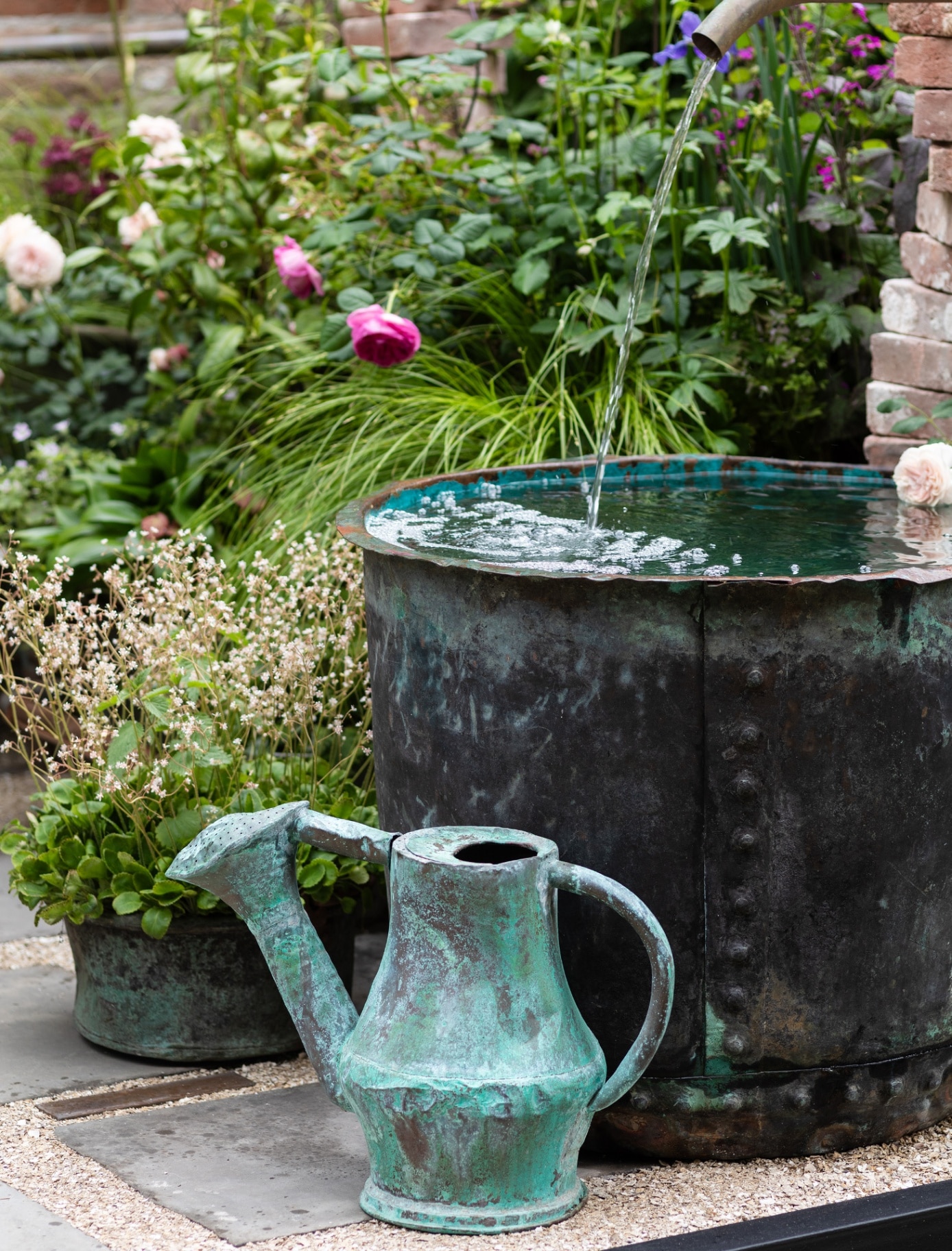 a blue metal jug on the floor and a large metal tub being filled with water from an outdoor tap