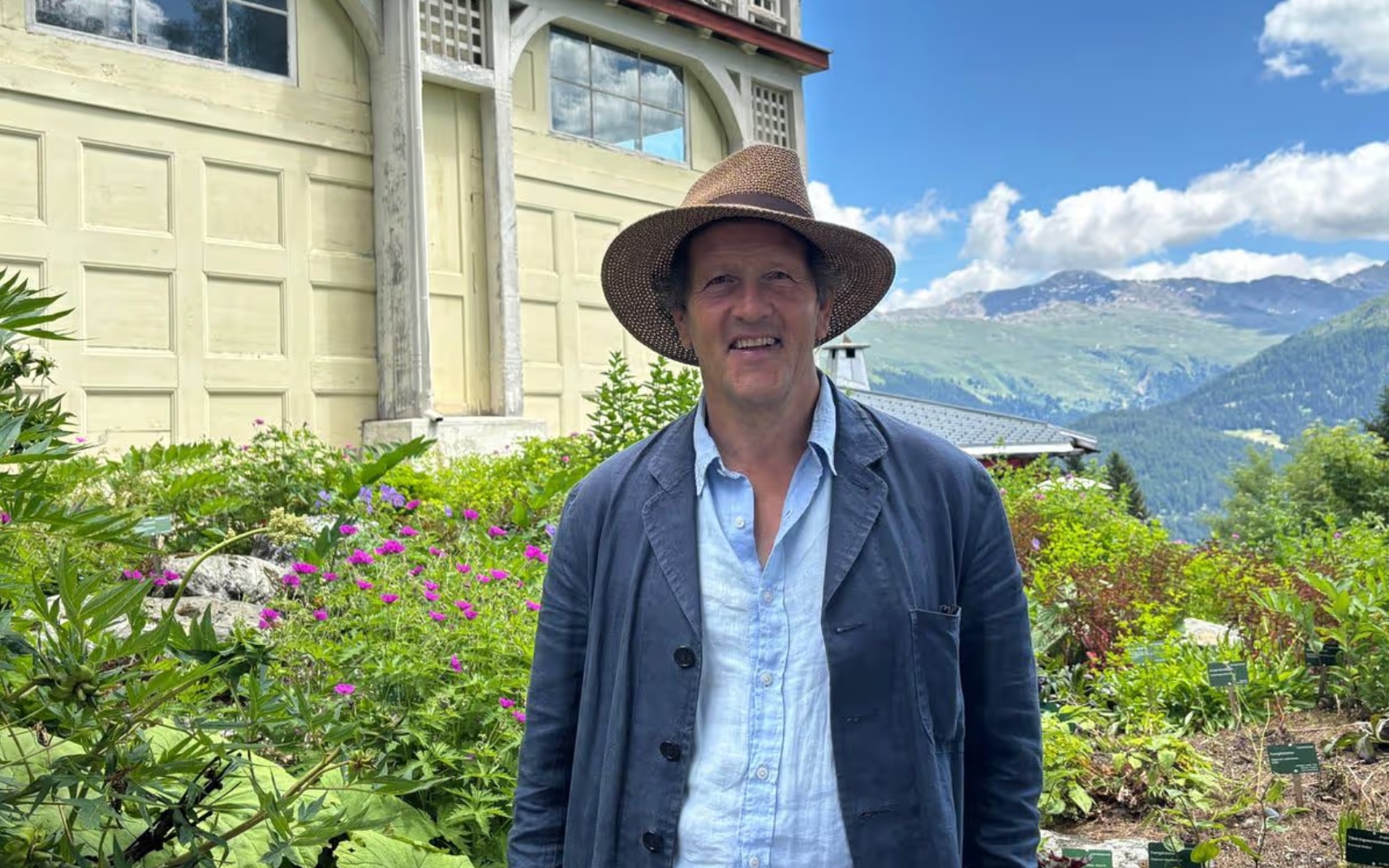 Monty Don pictured wearing a blue gardening jacket french coat smiling with a view of the hills along the rhine