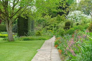 Scenic View of a Stone Paved Path trough a Grass Lawn and Flower Bed in a Beautiful Landscape Garden