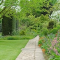 Scenic View of a Stone Paved Path trough a Grass Lawn and Flower Bed in a Beautiful Landscape Garden